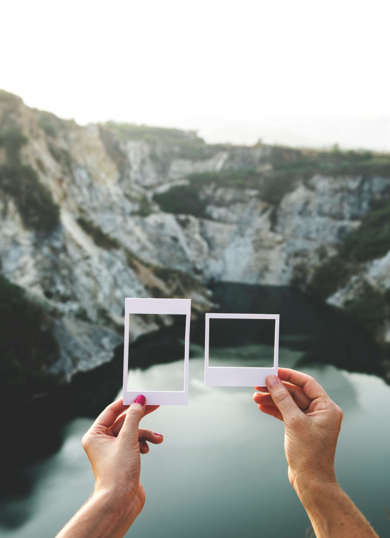 two hands holding up different sized pictures frames in front of mountain