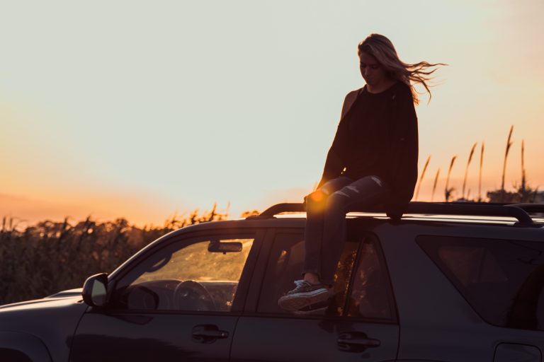lifestyle design woman sitting on car at sunset